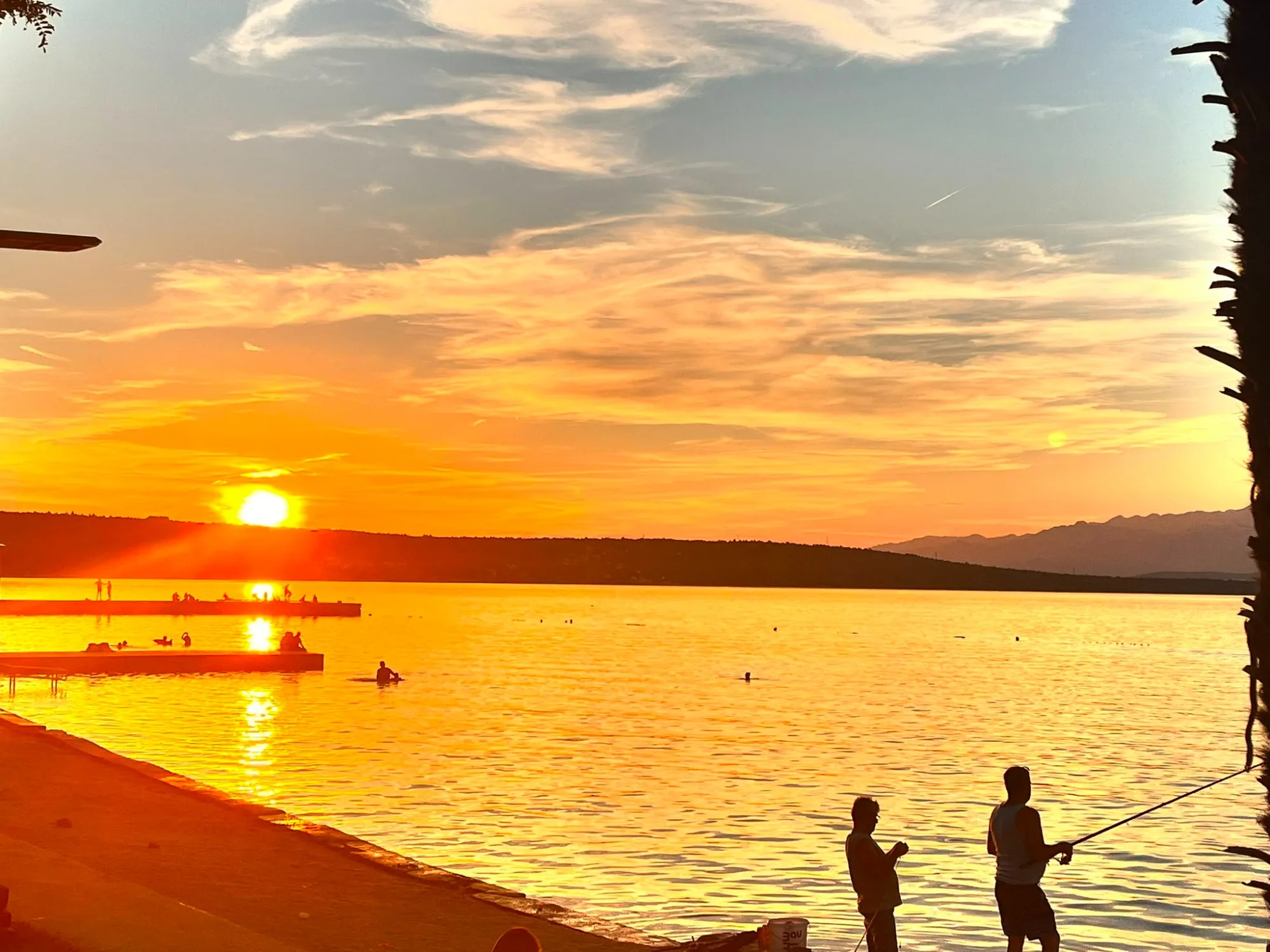 Sonnenuntergang am Karinsko More mit Schwimmern und Anglern am Ufer