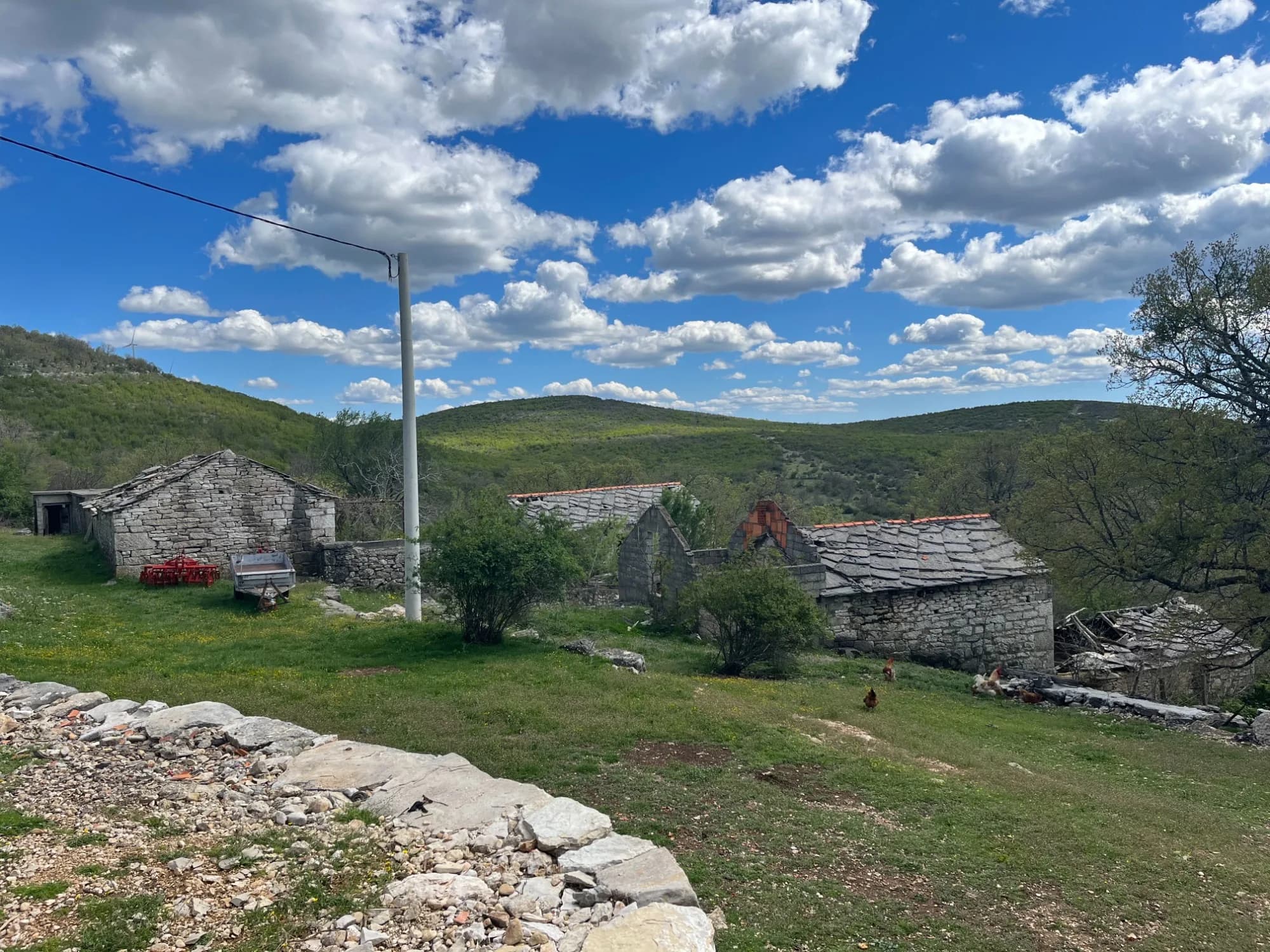 Verlassenes Steindorf mit Hühnern unter dramatischem Wolkenhimmel